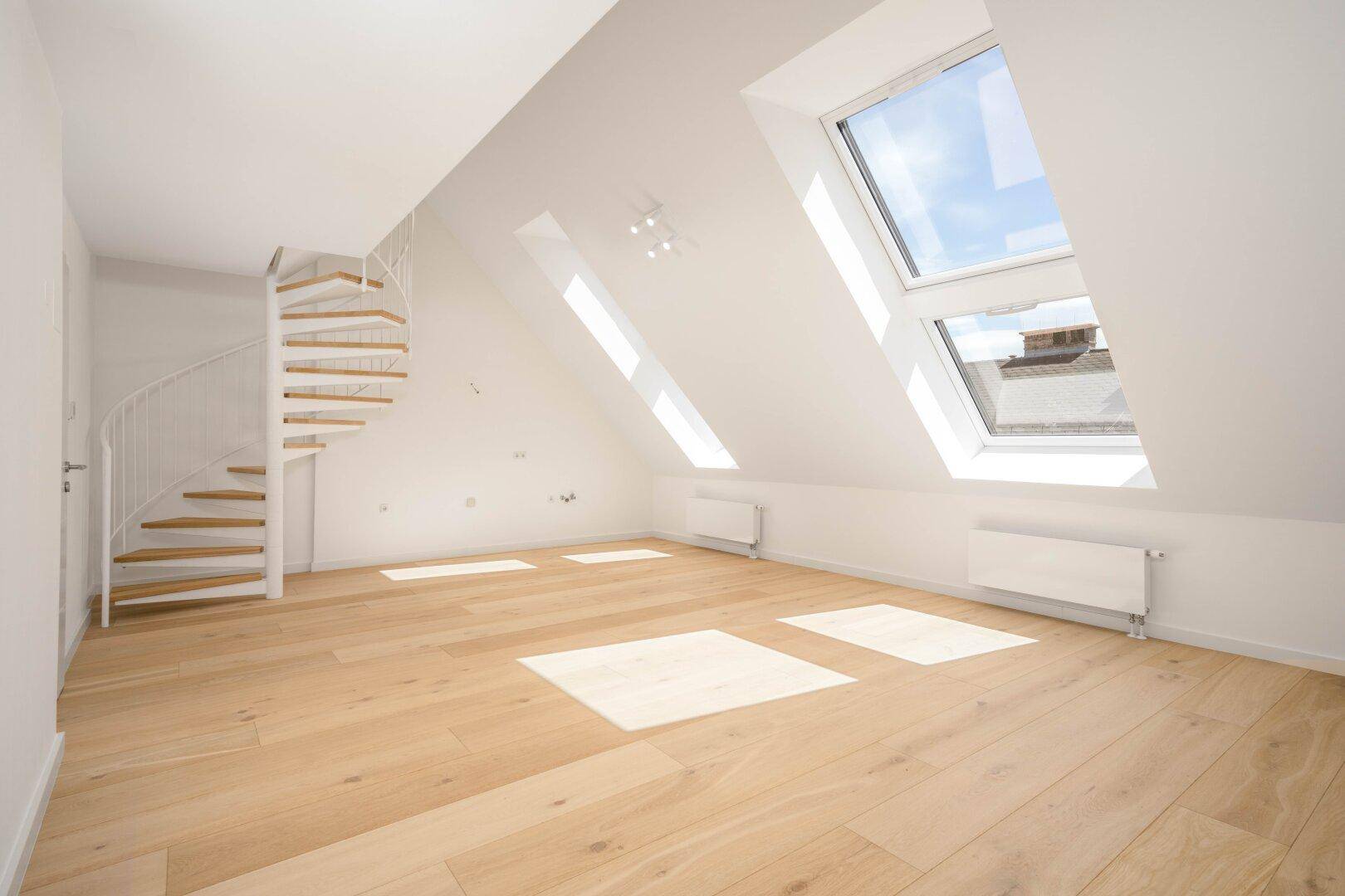 Heller Dachgeschossraum mit Holzboden, Wendeltreppe und großen Dachfenstern, einladend und offen.
