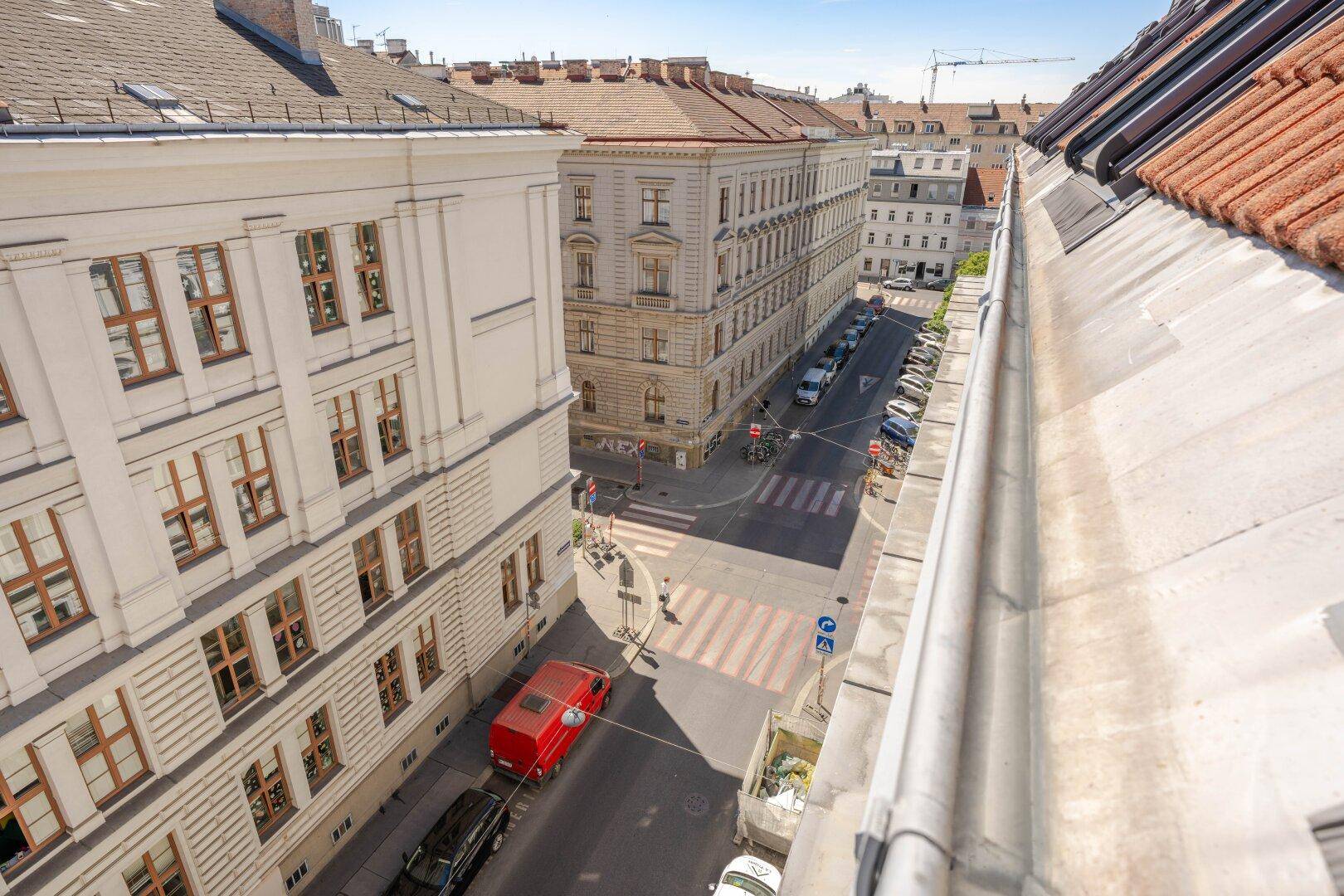 Blick von oben auf eine belebte Stadtstraße mit parkenden Autos und historischen Gebäuden.