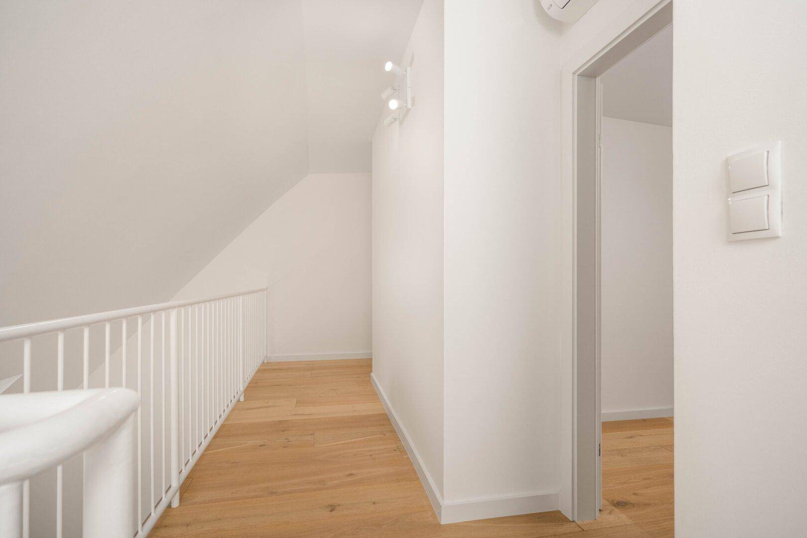 Heller Flur auf der Galerieebene mit Holzboden und weißem Geländer, modern und offen gestaltet.