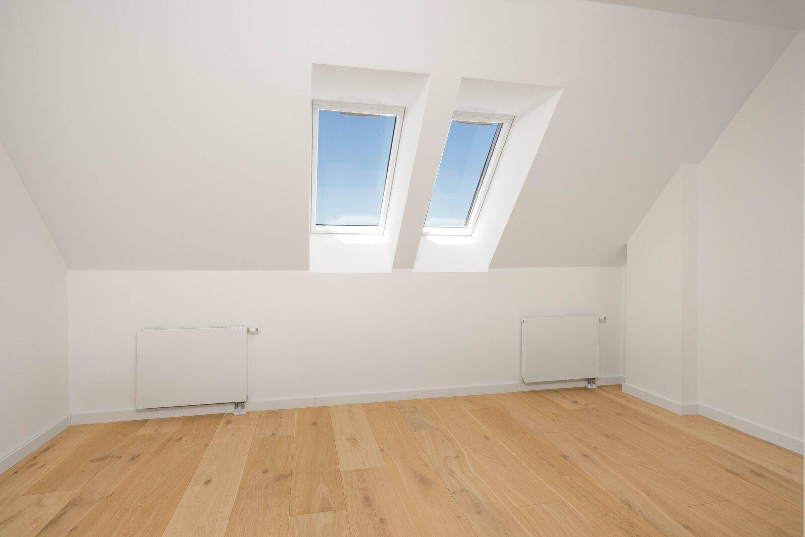 Helles Schlafzimmer im Dachgeschoss mit Holzboden und zwei Dachfenstern, gemütlich und ruhig.