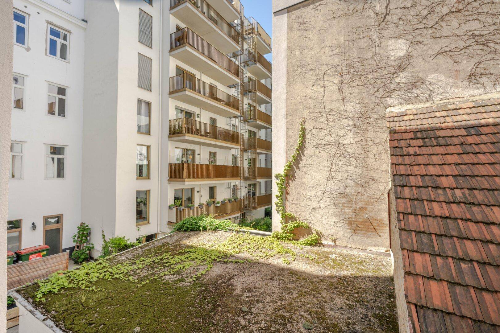 Blick in einen Innenhof mit begrünten Dächern und Balkonen eines angrenzenden Wohngebäudes.