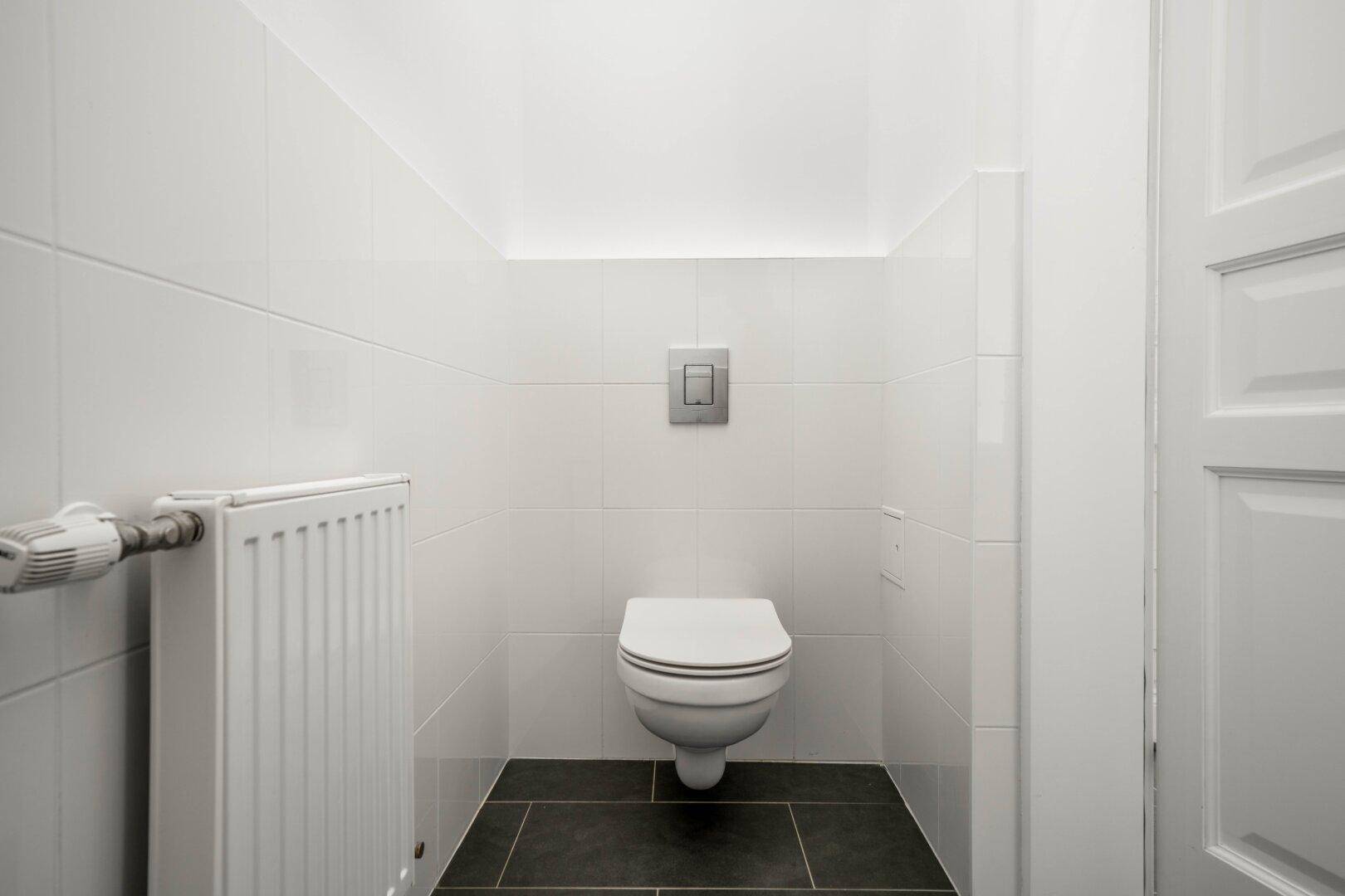 Modernes Gäste-WC mit weißen Wandfliesen, wandhängendem WC und Heizkörper.