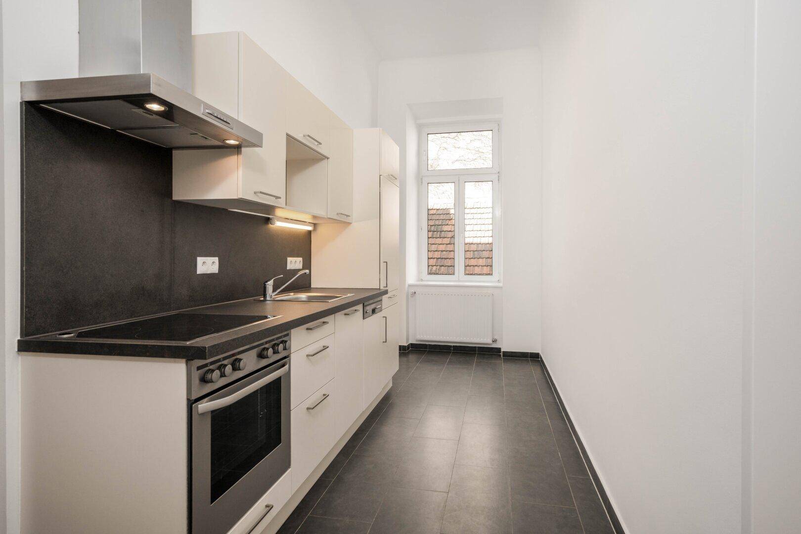 Moderne Küche mit hellen Schränken, Kochfeld und Dunstabzugshaube, ideal für eine kleine Wohnung.