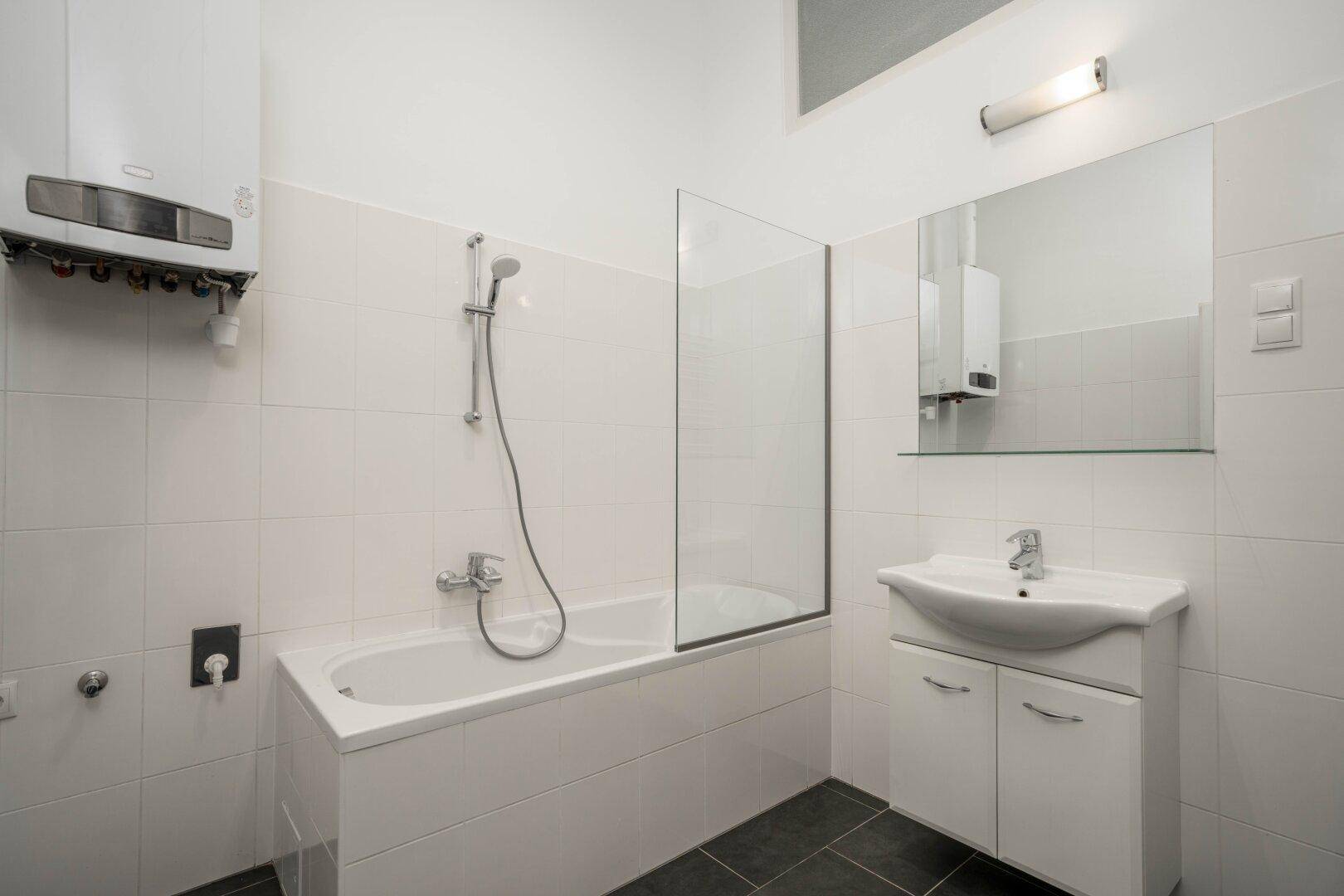 Badezimmer mit Badewanne, Duschabtrennung, Waschbecken und Gastherme an der Wand.