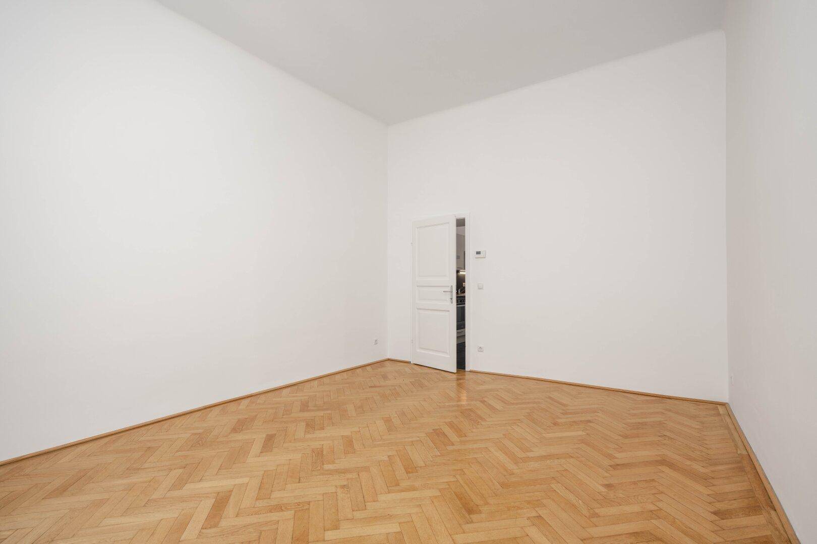 Leerer Raum mit Holzboden und weißer Tür, ideal für Schlaf- oder Wohnbereich.