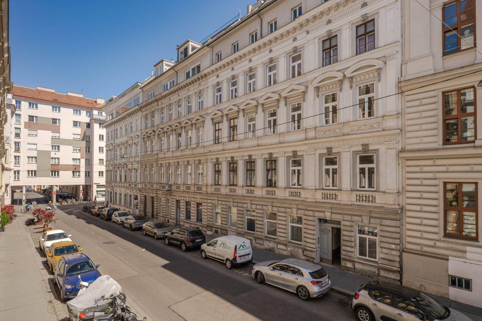 Panoramablick auf eine historische Stadtstraße mit eleganten Fassaden und parkenden Fahrzeugen.