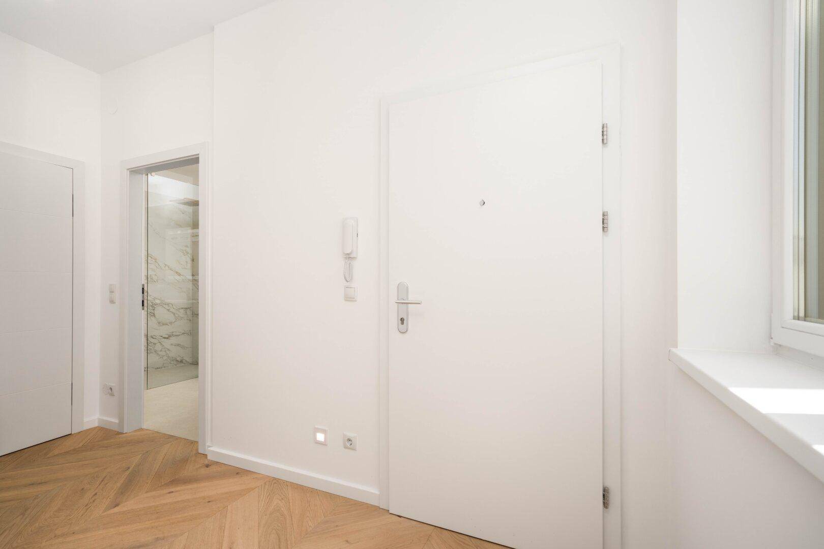 Moderner Flur mit Holzboden und weißer Eingangstür, die zu weiteren Räumen führt.