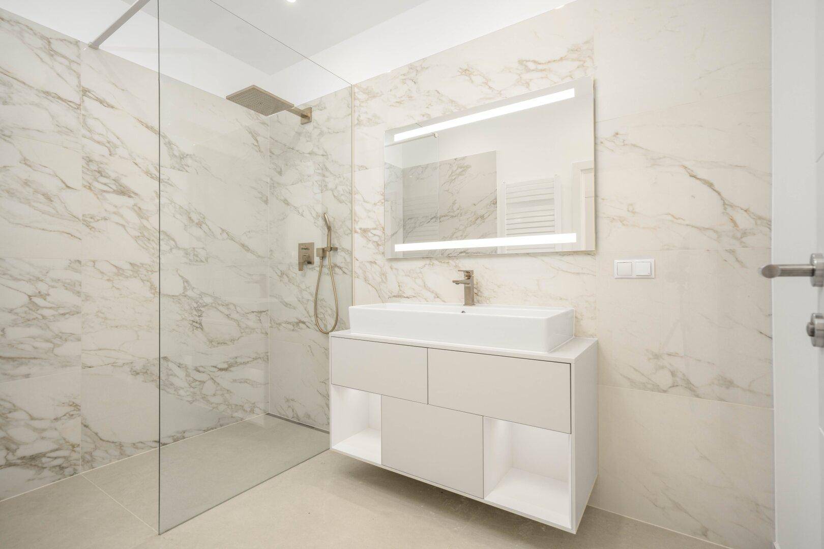 Elegantes Badezimmer mit Marmorfliesen, großer begehbarer Dusche und modernem Waschtisch.