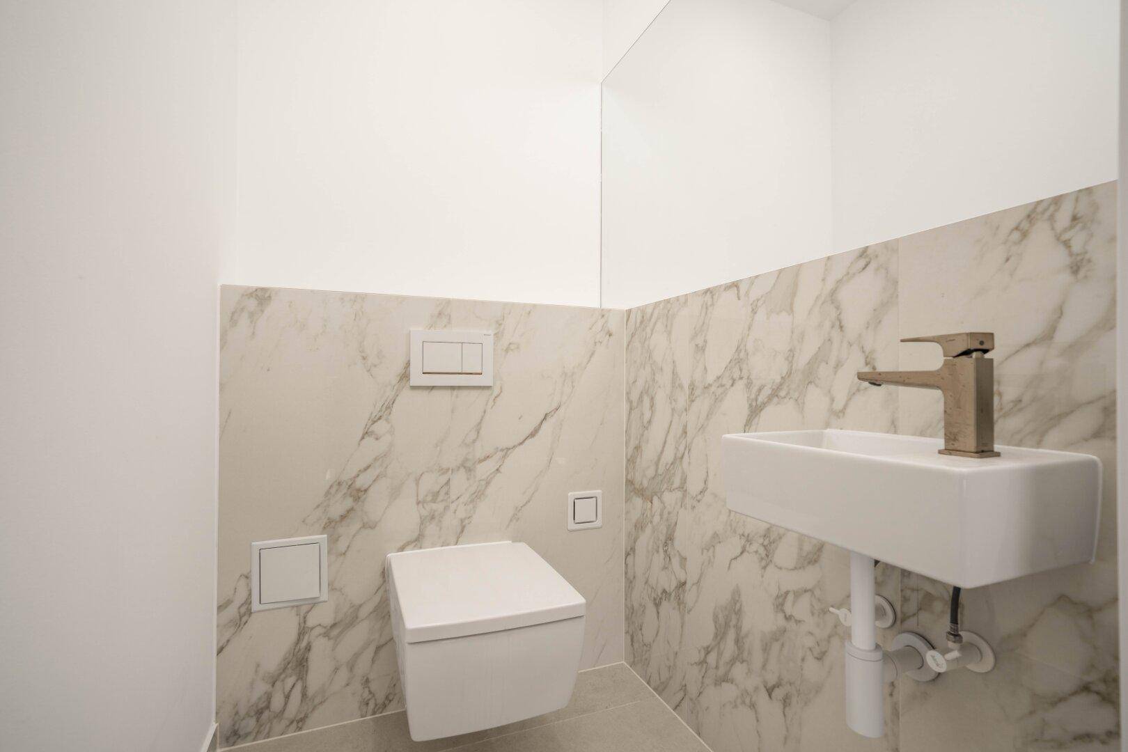 Modernes Gäste-WC mit Marmorfliesen, wandhängendem WC und kleinem Waschbecken.
