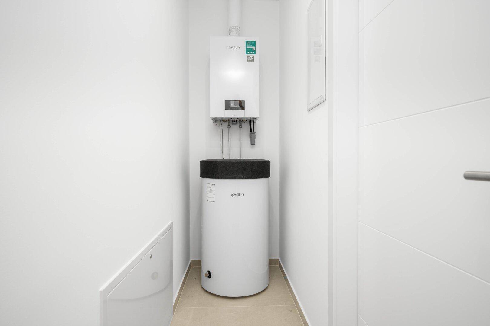 Kleiner Hauswirtschaftsraum mit Warmwasserbereiter und Heizungsanlage in weißer Umgebung.