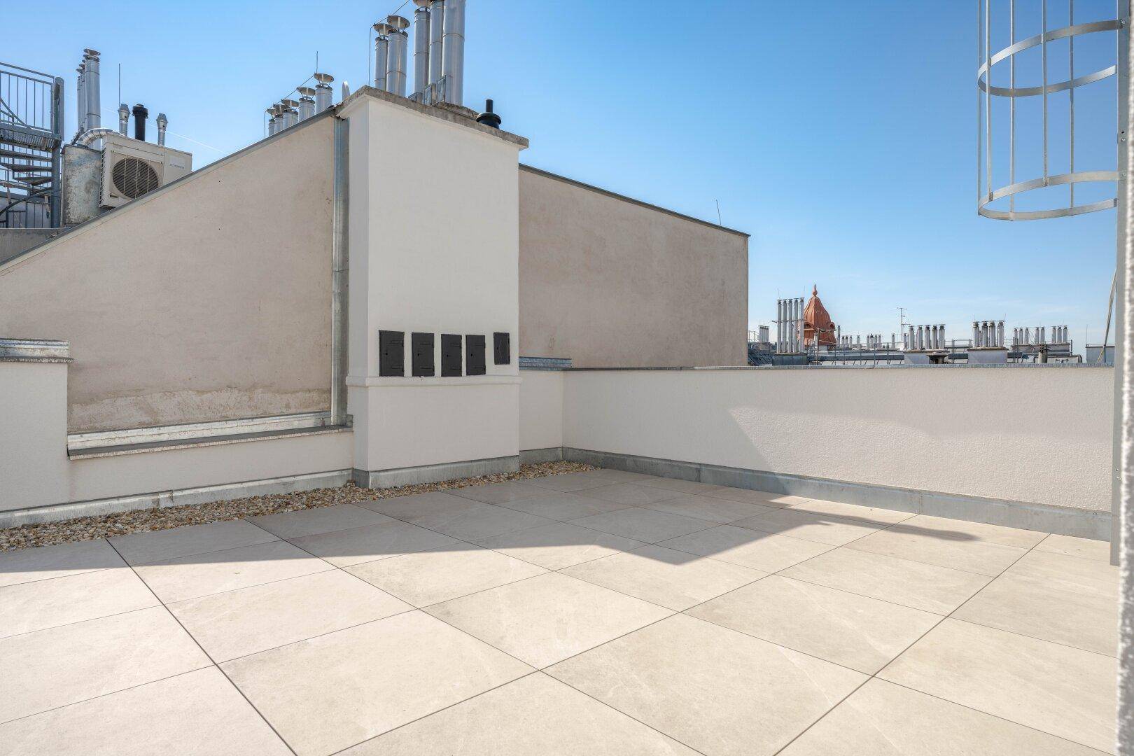 Geräumige Dachterrasse mit hellen Fliesen und Blick auf die umliegenden Dächer der Stadt.