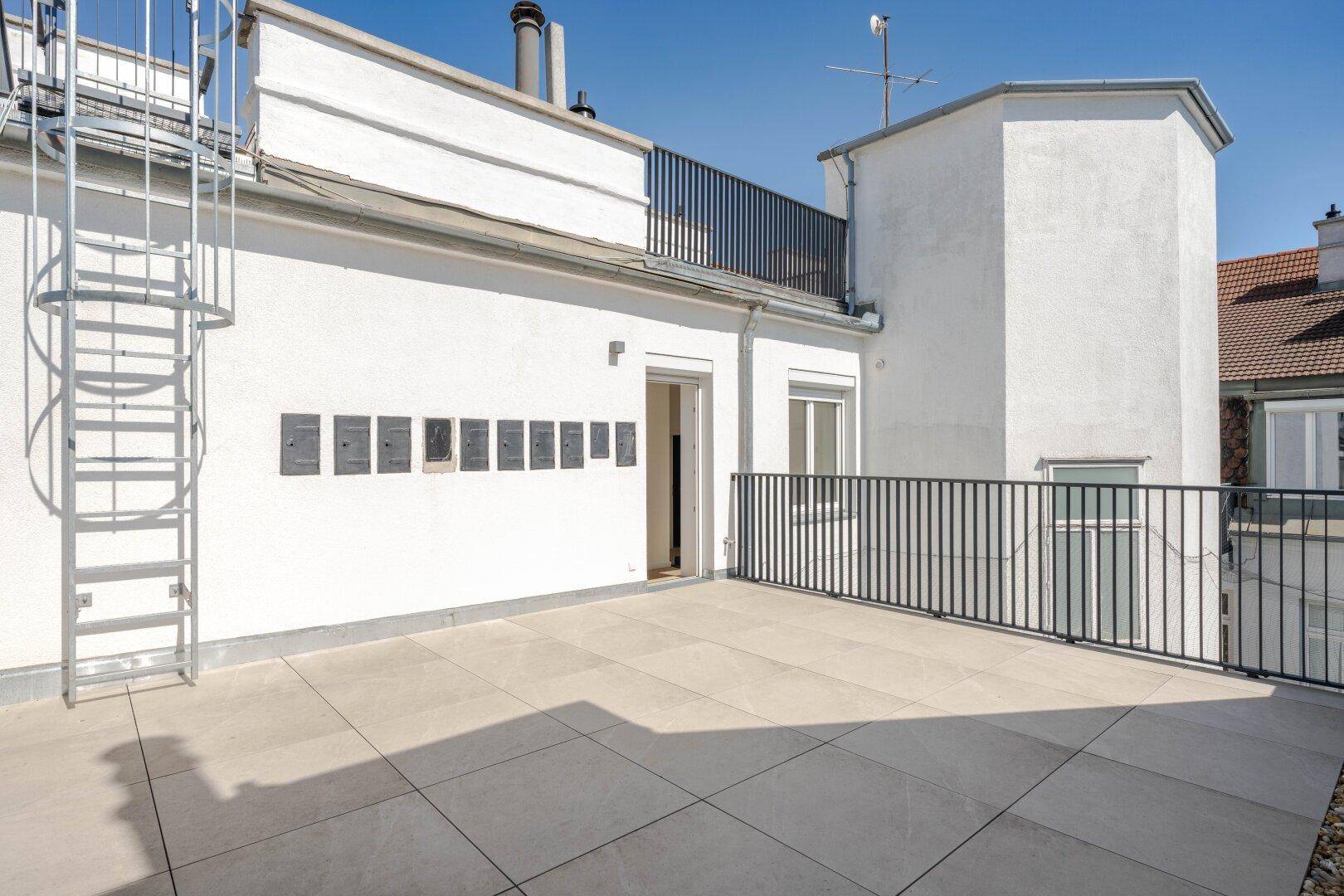 Weitläufige Dachterrasse mit Fliesenboden und schwarzem Geländer, ideal für Entspannung im Freien.