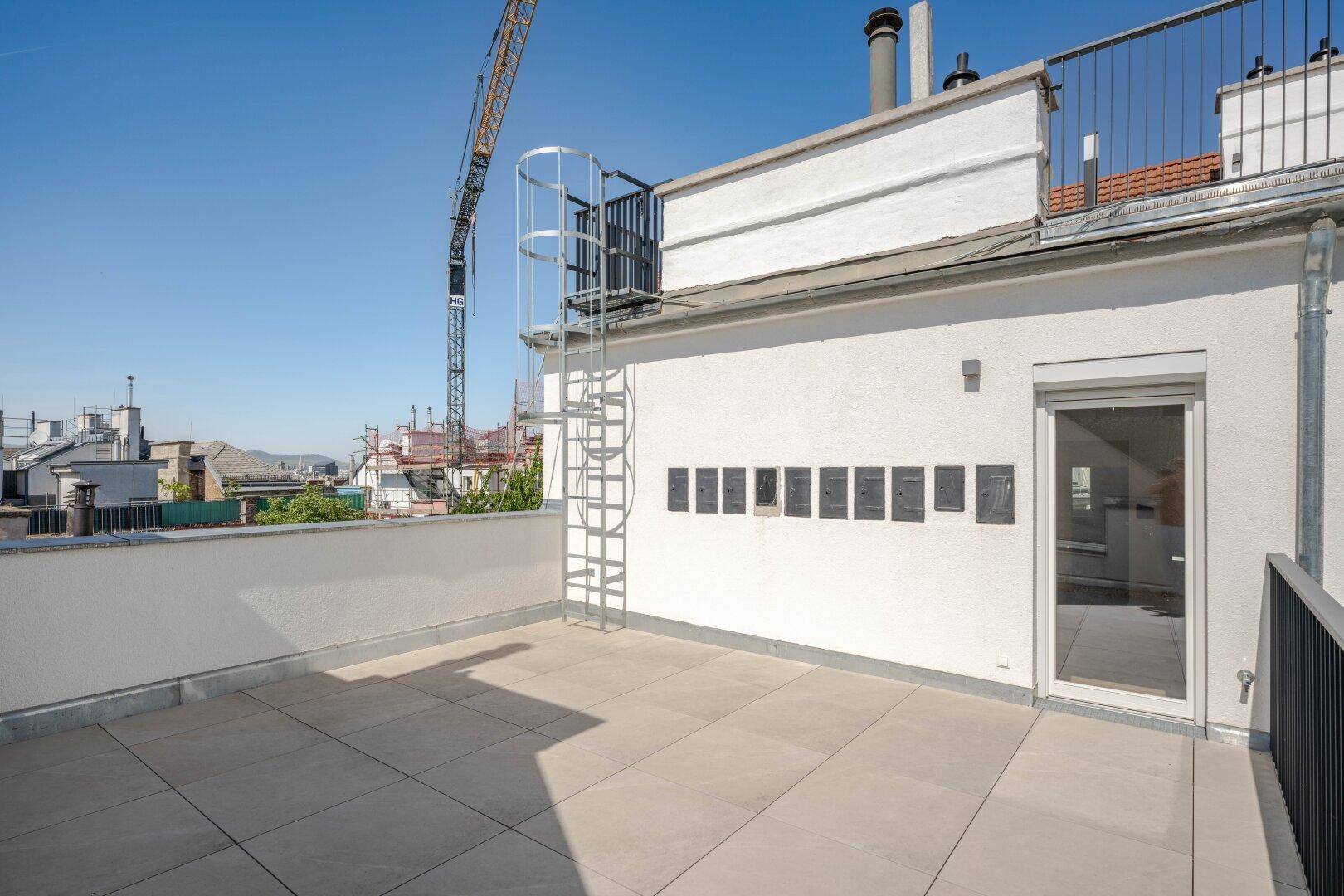 Sonnige Dachterrasse mit Fliesen und Blick auf die Stadt und einen Baukran in der Ferne.
