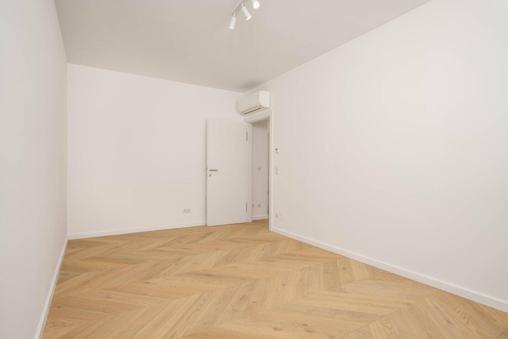 Leeres Zimmer mit Fischgrätparkett und Klimaanlage, bereit zur individuellen Gestaltung.