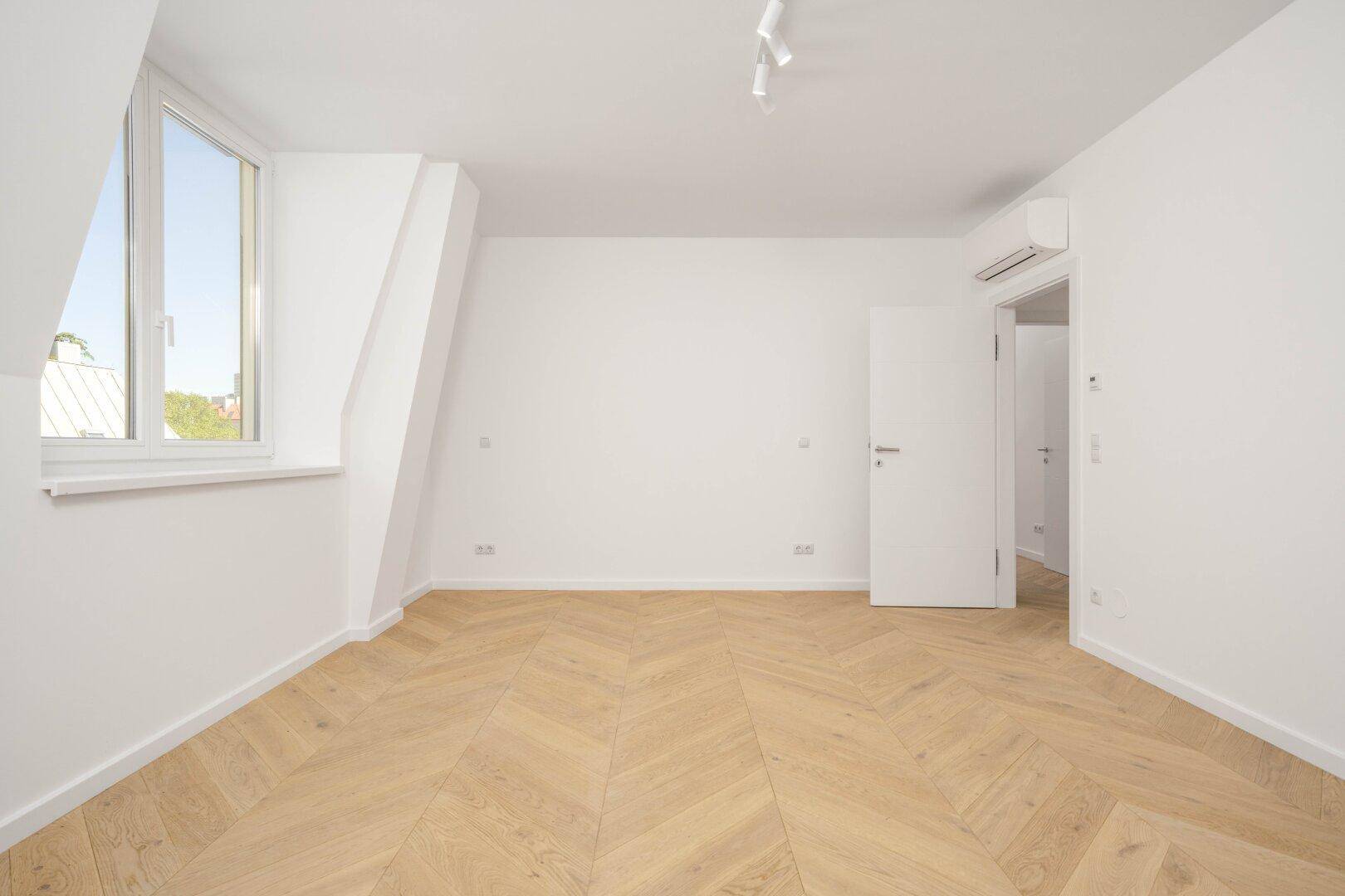 Helles Schlafzimmer mit Fischgrätparkett und Dachschräge, bietet viel natürliches Licht und Klimaanlage.