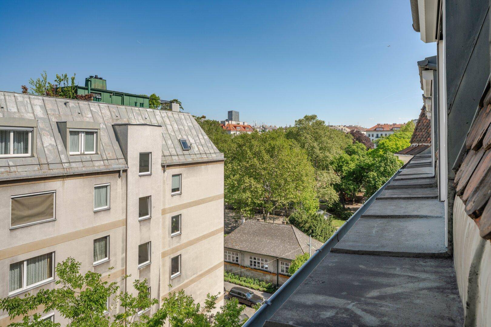 Gebäudefassade mit Blick auf grüne Bäume und die umliegende Stadtlandschaft unter blauem Himmel.