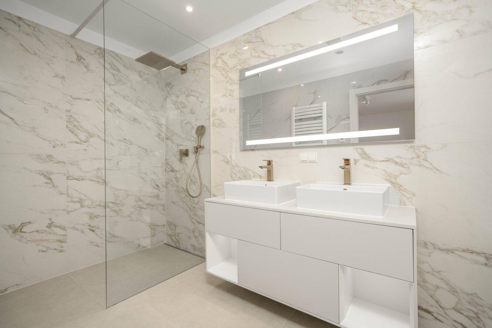 Luxuriöses Badezimmer mit Marmorfliesen, großer Dusche und Doppelwaschbecken.