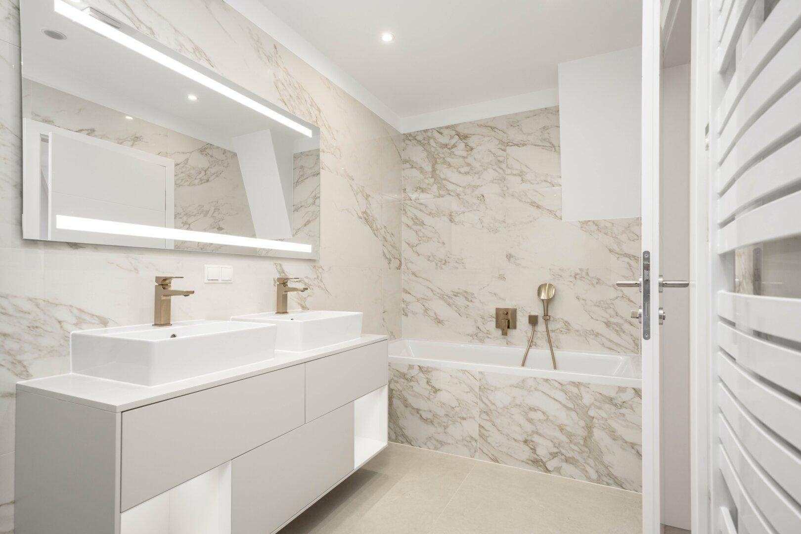 Modernes Badezimmer mit doppelten Waschbecken, Badewanne und eleganten Marmorfliesen an den Wänden.