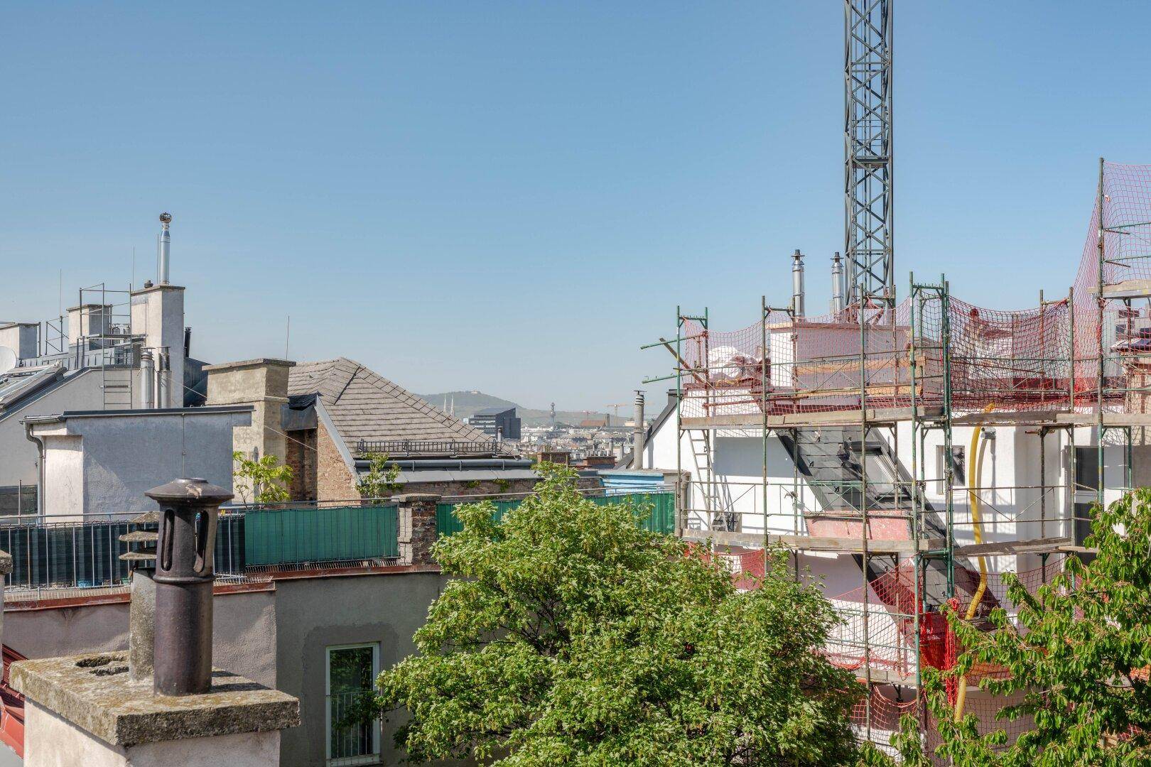 Blick über städtische Dächer mit einer Baustelle und einem Kran im Hintergrund unter blauem Himmel.