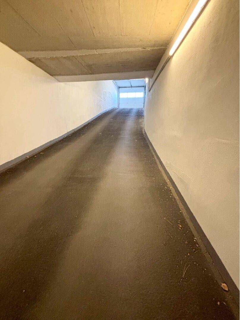 Zufahrtsrampe zur Tiefgarage mit hellen Wänden und Beleuchtung.