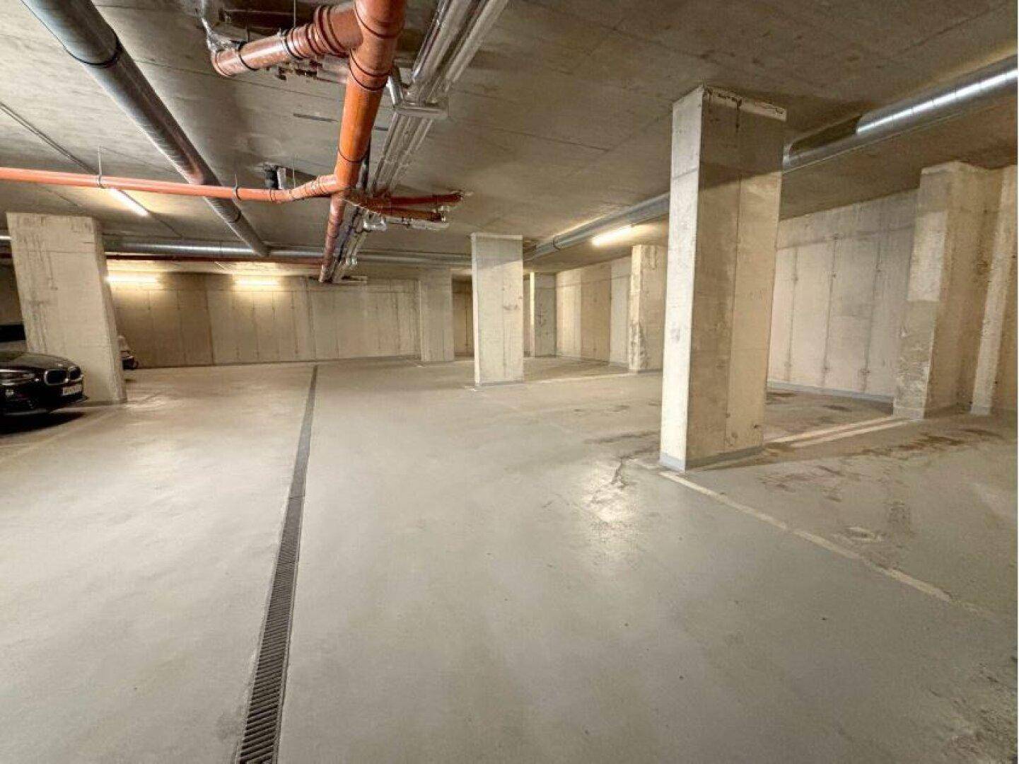 Weitläufige Tiefgarage mit vielen Stellplätzen, Betonpfeilern und Deckeninstallationen.