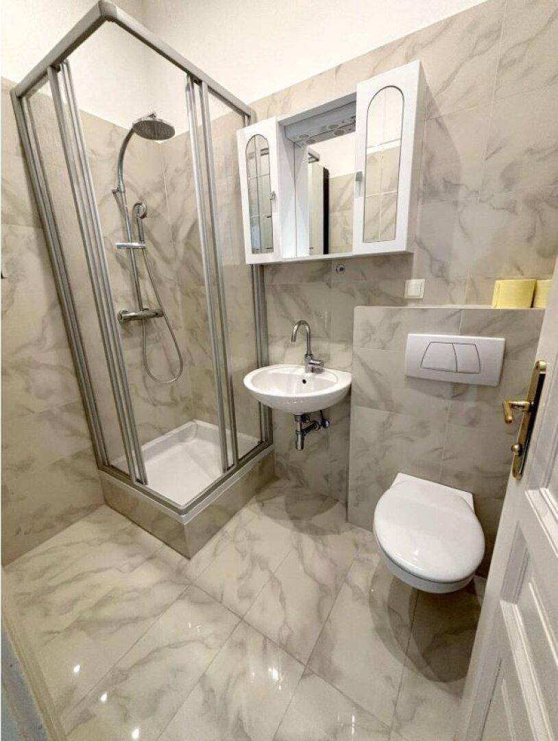 Modernes Badezimmer mit Duschkabine, wandhängendem WC und Waschbecken, komplett gefliest in hellem Marmor-Look.