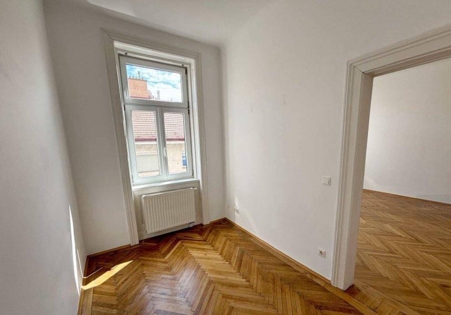 Kleinerer Raum mit Fischgrätparkett, einem Fenster und weiß gestrichenen Wänden, ideal als Arbeitszimmer.