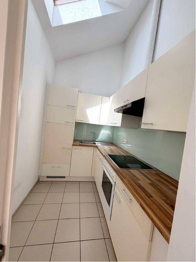 Moderne Küche mit weißen Schränken, Holz-Arbeitsplatten, Fliesenboden und einem Dachfenster.