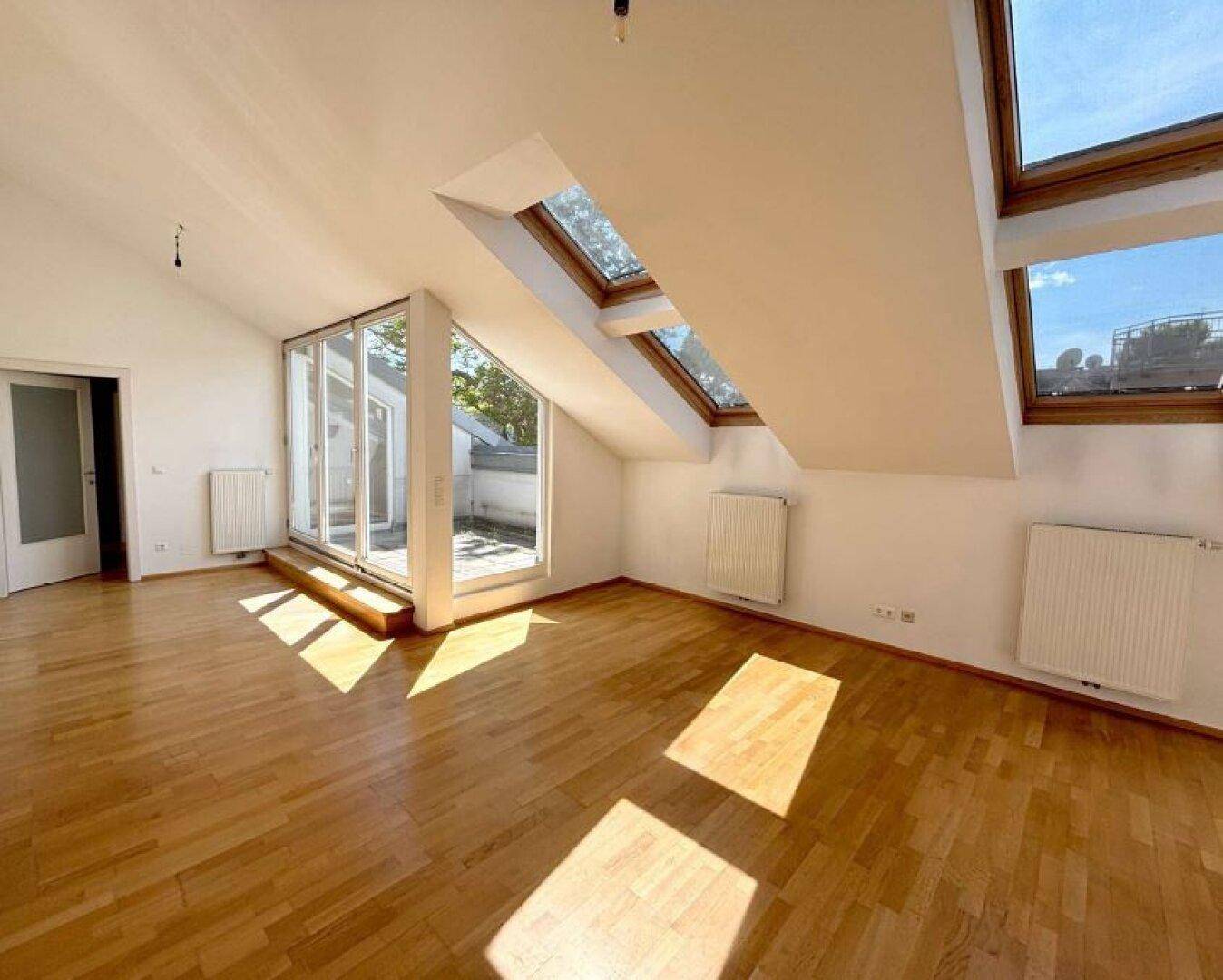 Geräumiges Zimmer mit Parkettboden, Dachschrägen und mehreren Dachfenstern für viel Tageslicht.