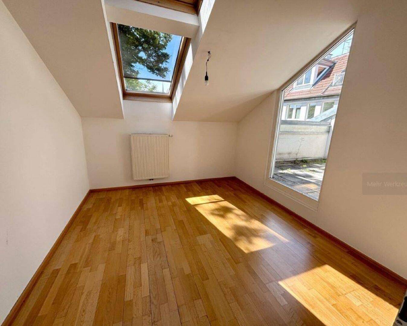 Helles Zimmer mit Parkettboden, Dachschräge und einem großen Dachfenster für natürliche Belichtung.