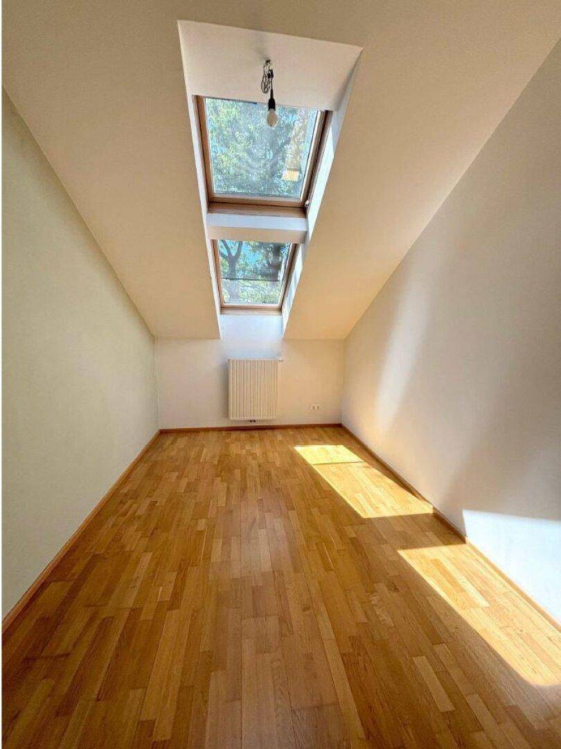 Helles Zimmer mit Parkettboden, Dachschrägen und zwei großen Dachfenstern für viel Licht.
