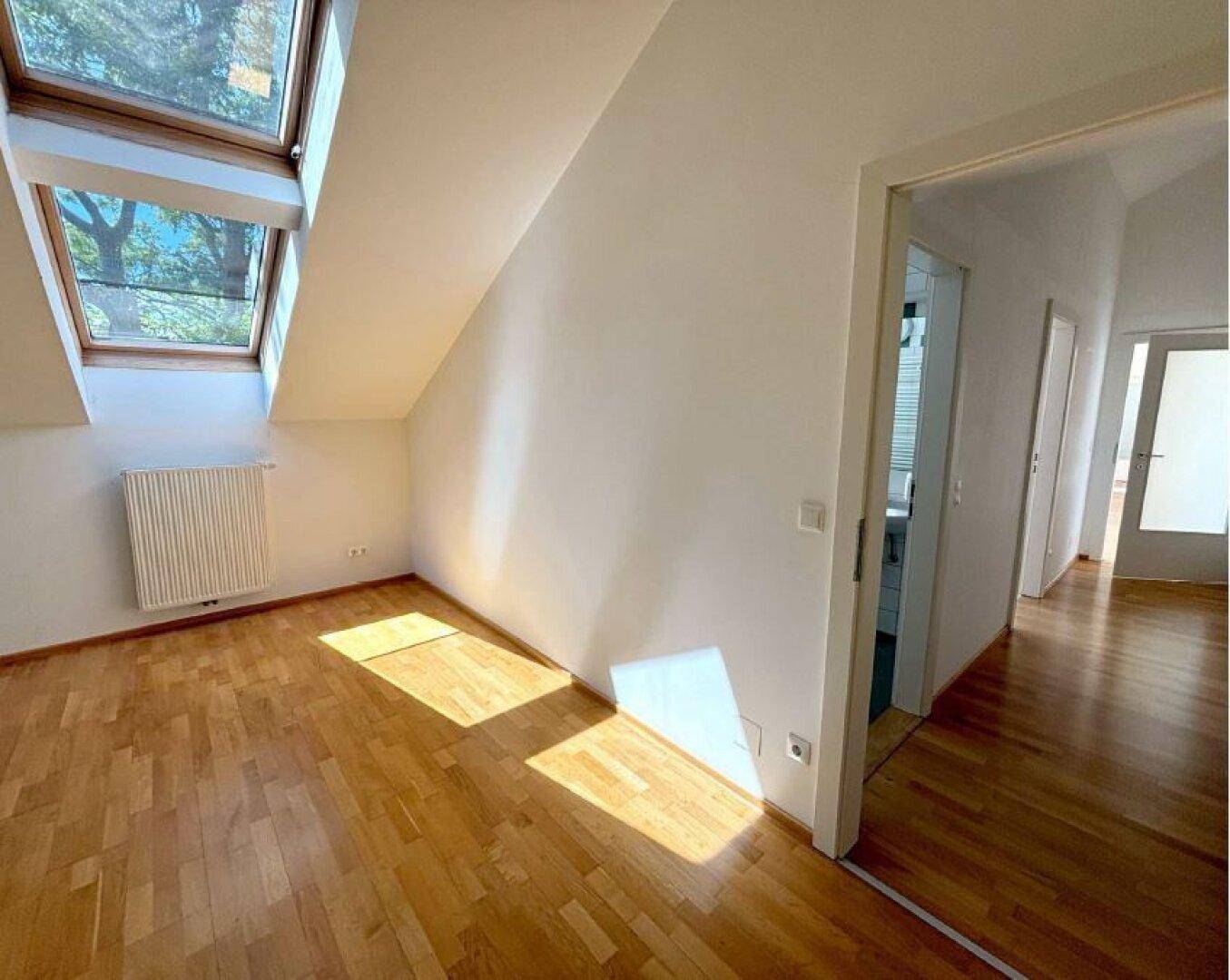 Geräumiges Zimmer mit Parkettboden, Dachschrägen und Dachfenstern, offen zum Flurbereich.