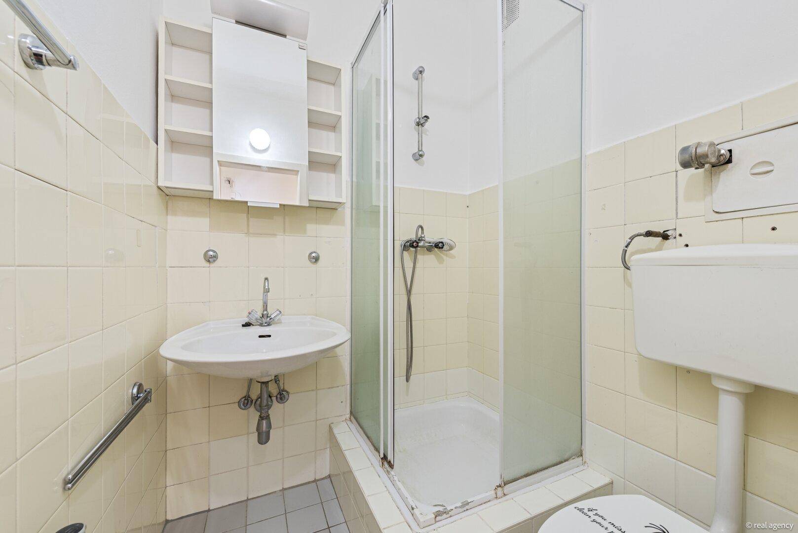 Badezimmer mit beigefarbenen Fliesen, Waschbecken, Duschkabine und Toilette, im älteren Stil gehalten.
