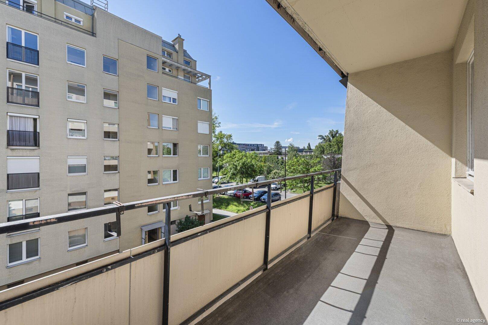 Langer Balkon mit Metallgeländer bietet einen weiten Blick über den begrünten Innenhof und die Umgebung.