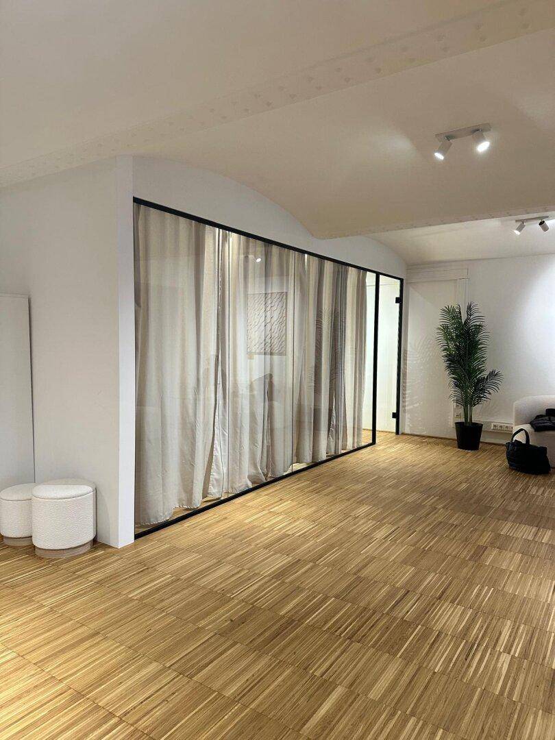 Moderner Gewerberaum mit Glaswand und Vorhängen, schafft flexible Bereiche und eine helle Atmosphäre.