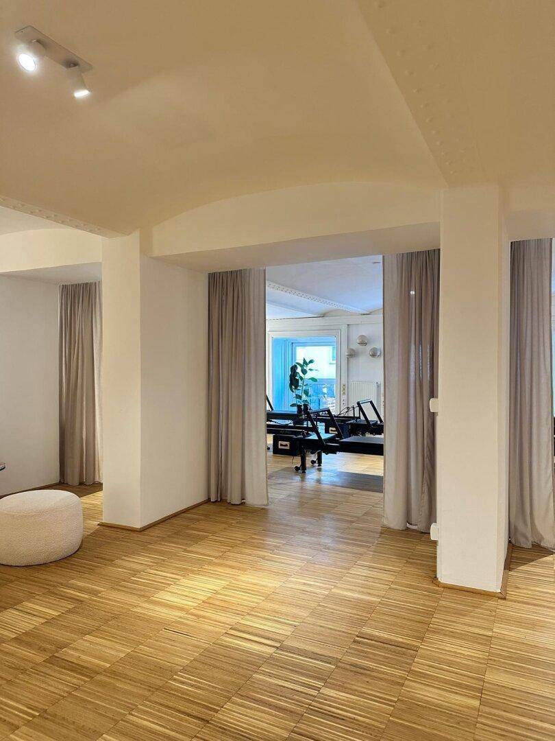 Blick in einen weiteren Bereich des Gewerberaums mit Pilates-Geräten, abgetrennt durch elegante Vorhänge.