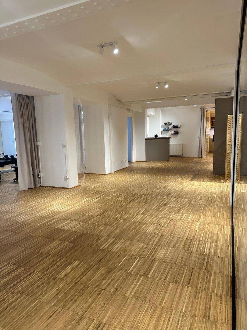 Weitläufiger Gewerberaum mit Parkettboden, Empfangstheke und moderner Glasabtrennung, bietet flexible Gestaltungsmöglichkeiten.