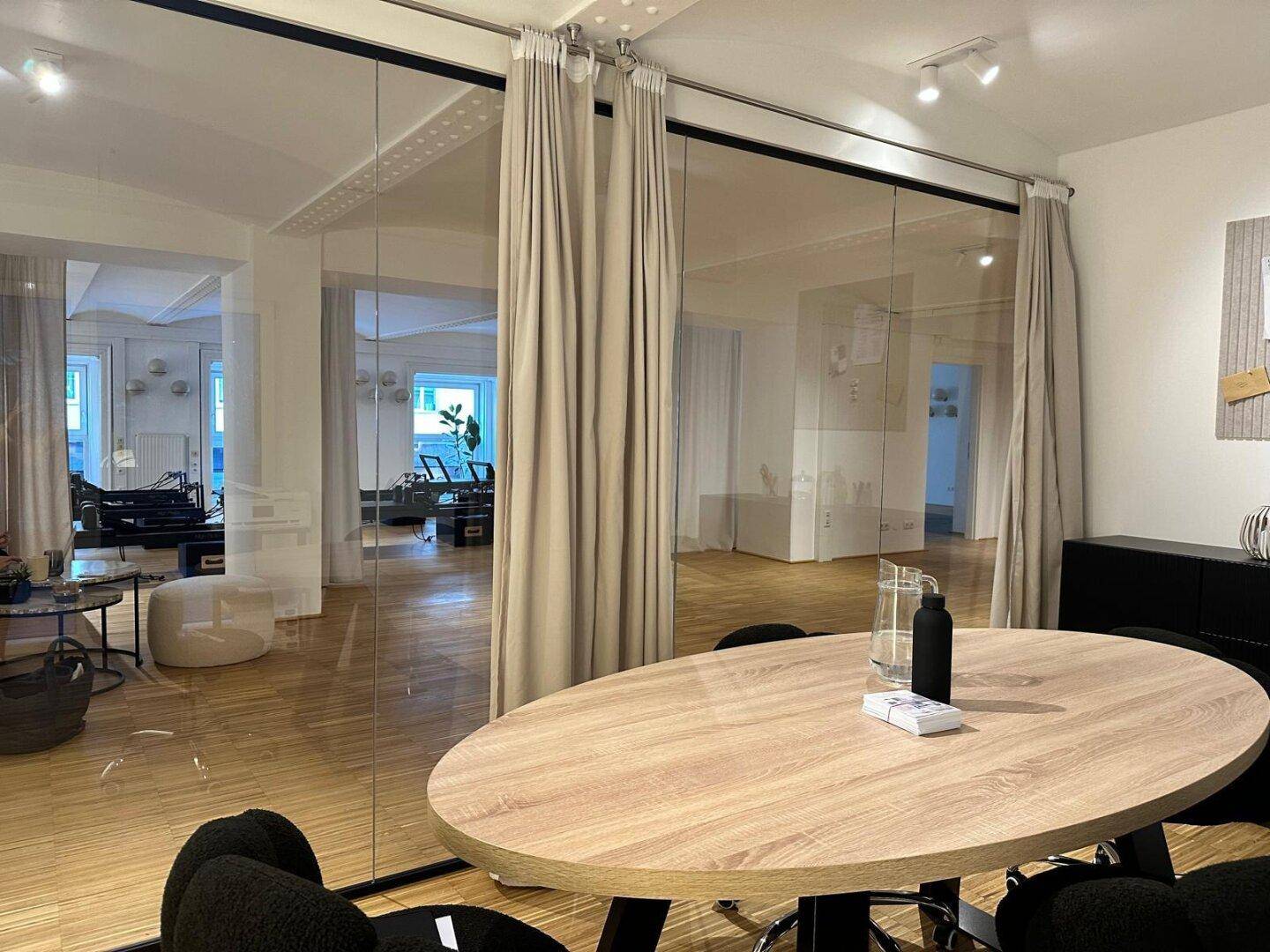 Büro mit Holztisch und Blick durch die Glasabtrennung in den hellen Hauptraum, ideal für Besprechungen.