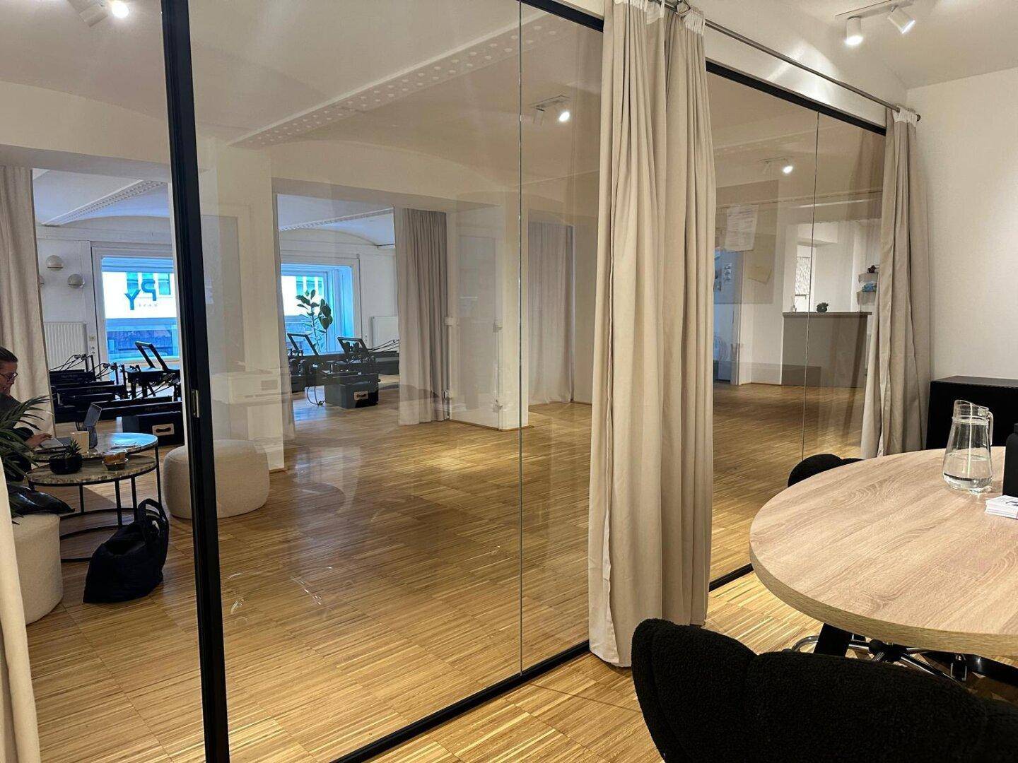 Blick vom Büro durch eine Glaswand in den Hauptgewerberaum mit Trainingsgeräten, schafft Transparenz und Verbindung.