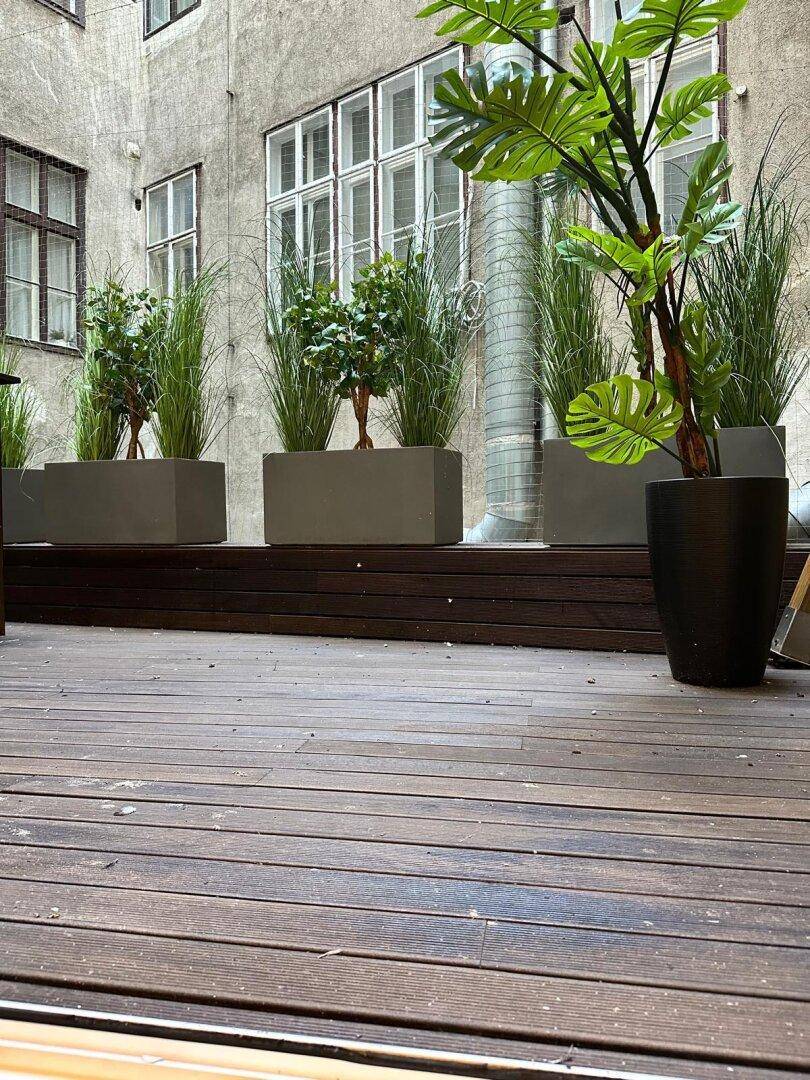 Attraktive Holzterrasse mit großen Pflanzkübeln und üppigem Grün, bietet einen ruhigen Außenbereich.