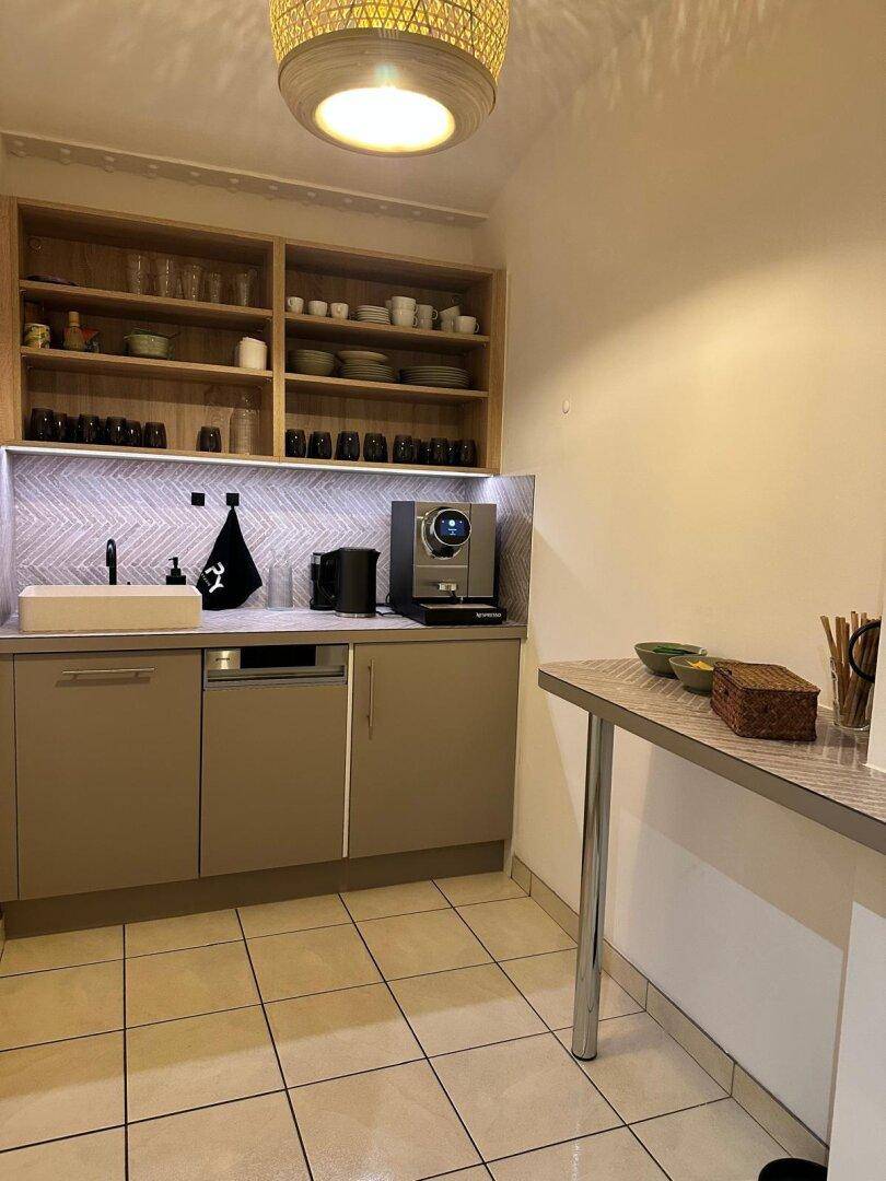 Funktionale Teeküche mit Spüle, Kaffeemaschine und offenem Regal, ideal für Pausen und kleine Mahlzeiten.