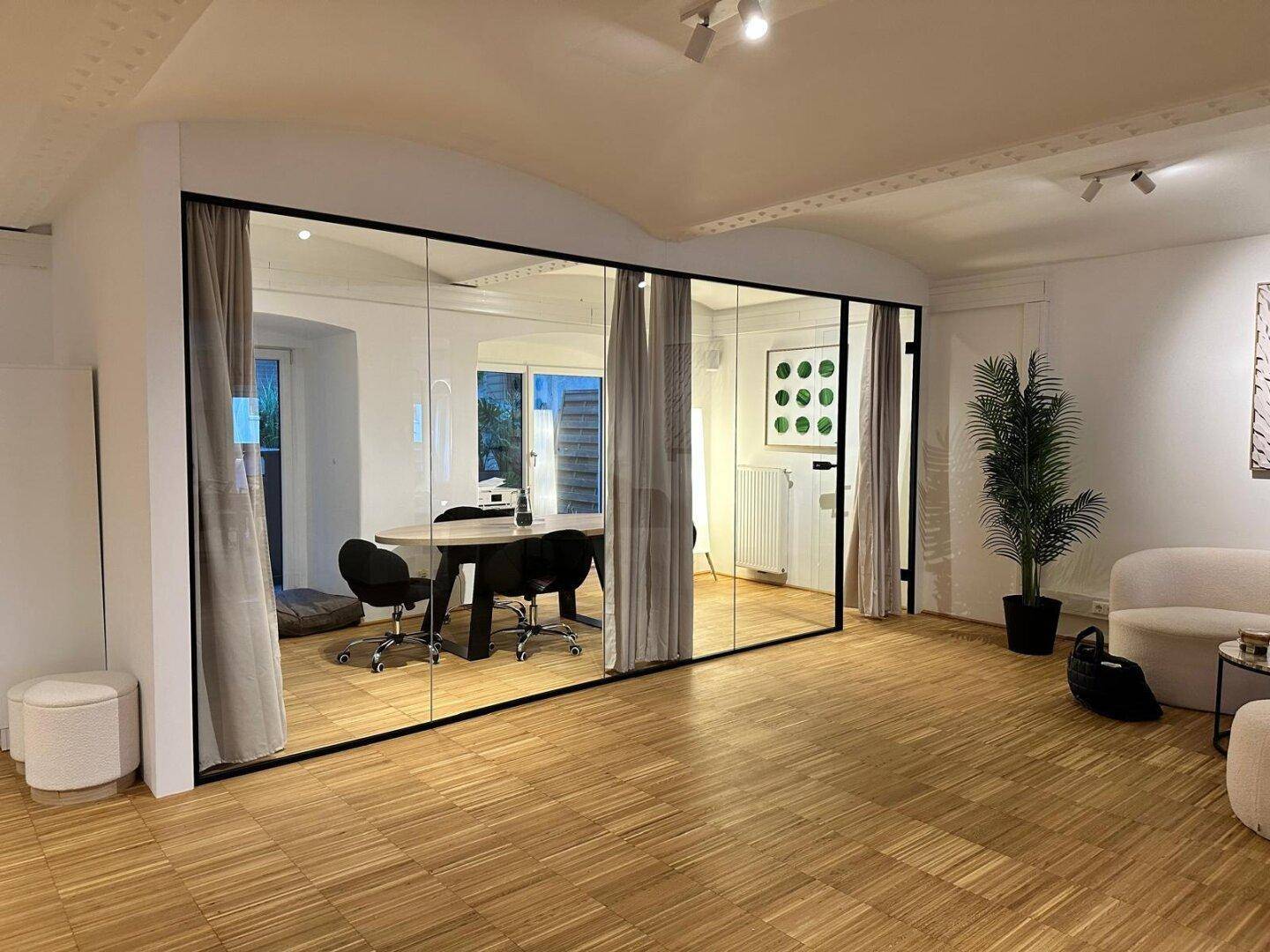 Blick in den Besprechungsraum durch die Glaswand, mit Holztisch und Pflanzen, schafft eine professionelle Umgebung.