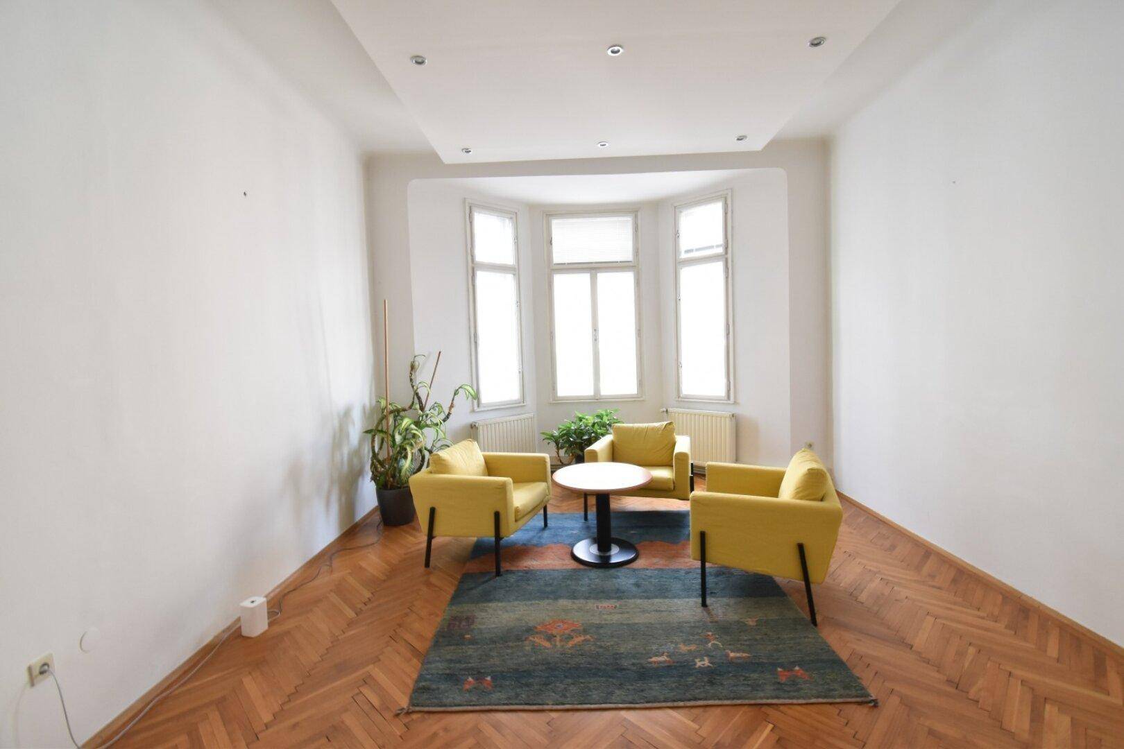 Helles Büro mit Erkerfenstern, Fischgrätparkett und drei gelben Sesseln um einen kleinen Tisch.