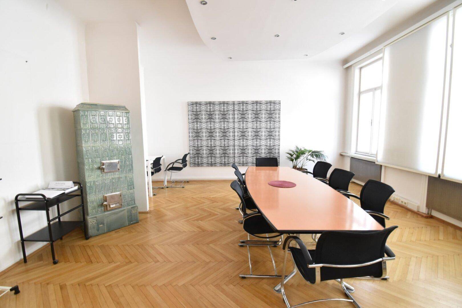 Großer Konferenzraum mit langem Tisch, vielen Stühlen, Kachelofen und großen Fenstern.