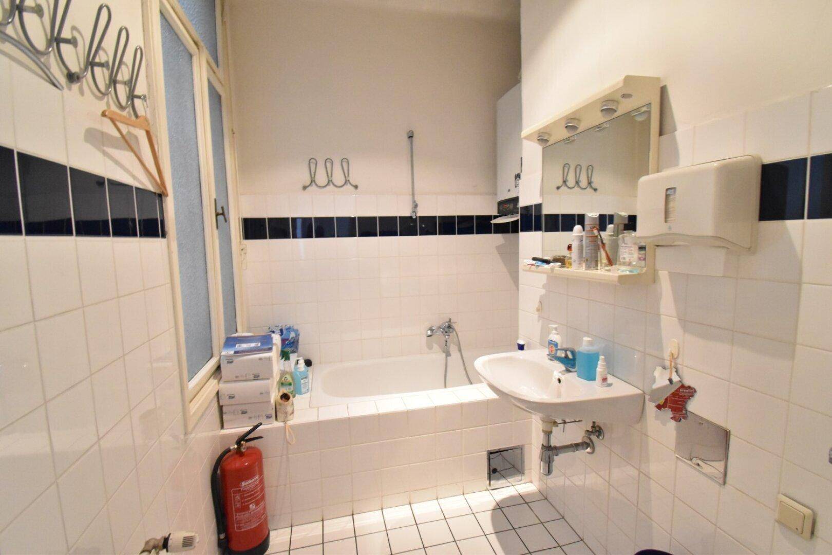 Kleines Badezimmer mit Badewanne, Waschbecken und weißen Fliesen, akzentuiert durch eine dunkle Bordüre.