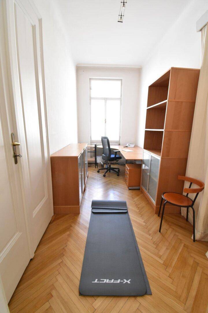 Schmaler Büroraum mit Holzregalen, Schreibtisch und einem Fenster, das Tageslicht hereinlässt.