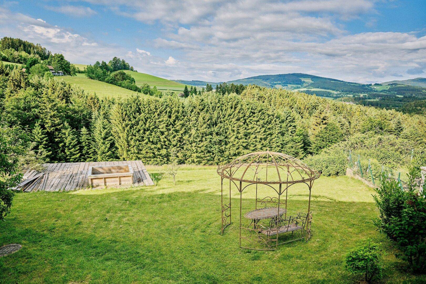 Weitläufiger Garten mit Pavillon, Holzterrasse und Panoramablick auf die bewaldeten Hügel.