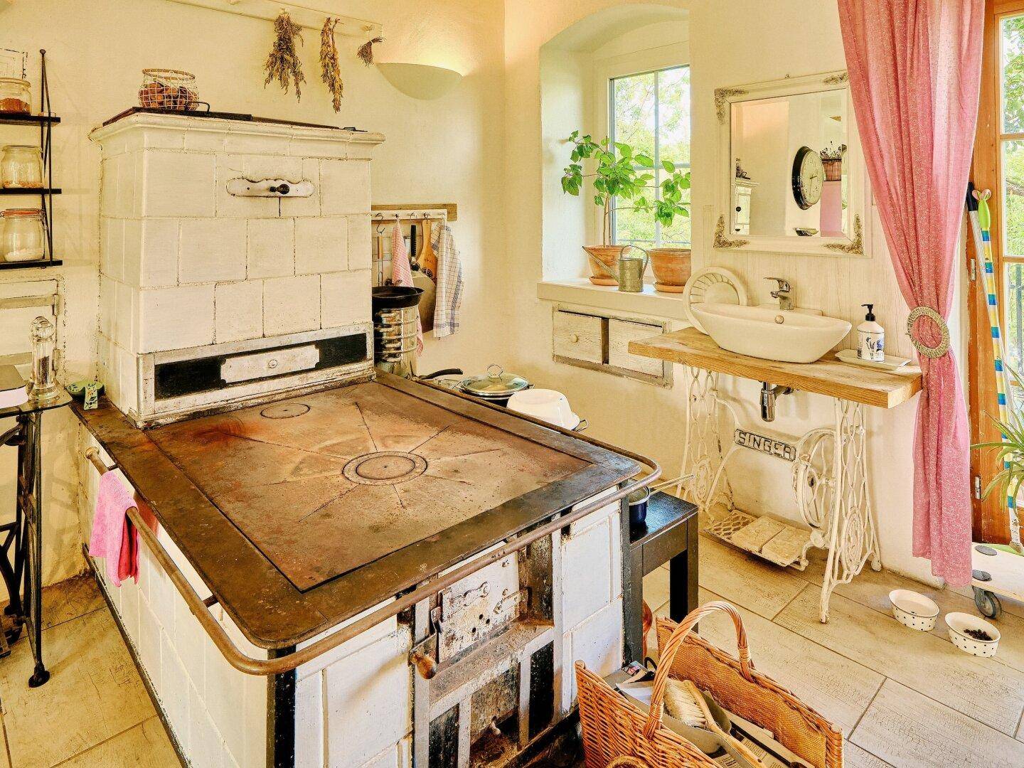 Detailansicht der Küche mit traditionellem Kachelofen, Vintage-Waschbecken und Fensterblick.