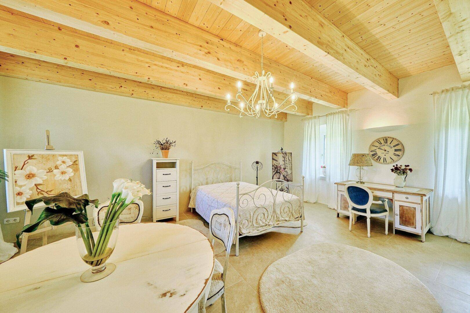 Helles Schlafzimmer mit Holzbalkendecke, schmiedeeisernem Bett und eleganten Möbeln.