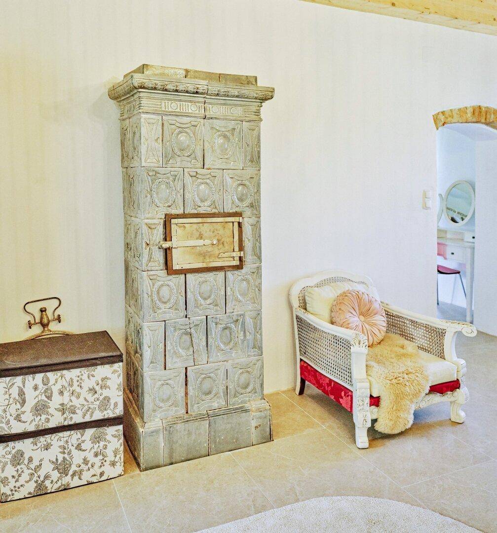 Schlafzimmer mit traditionellem Kachelofen, gemütlichem Sessel und rustikalen Details.